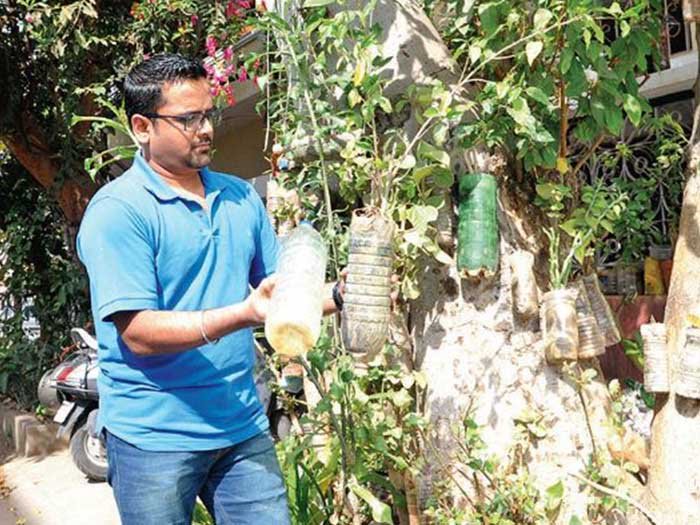 Environmentalist Sadhan Radhakrishnan holding bottled saplings in his hands against the background of his garden