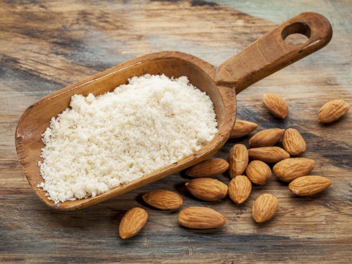 Fresh almond powder in a wooden spoon with loose almonds scattered