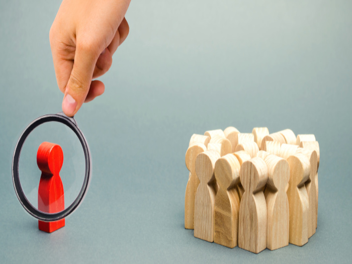 Group of wood figurines huddled together with one figure outside the group.