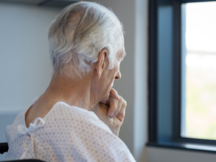 An older man sitting in a hospital robe looking out the window