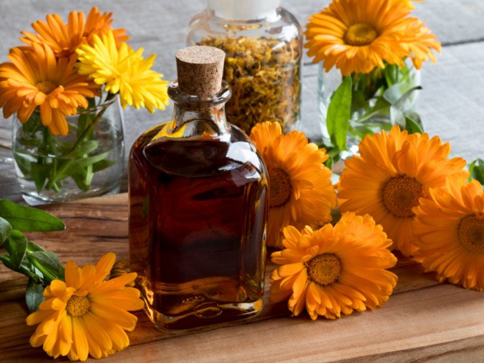 A small jar of calendula oil with calendula flowers on a wooden table