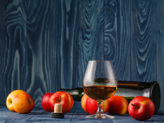 A wine glass with calvados next to apples on a table counter