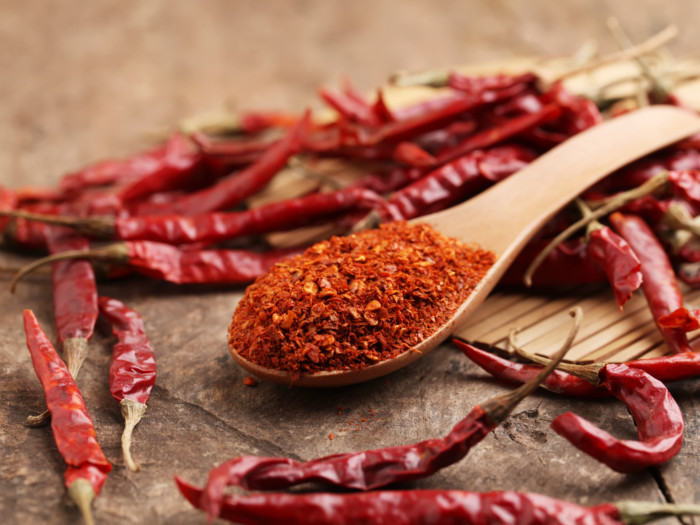 Crushed cayenne pepper in a wooden spoon with red chillis placed around