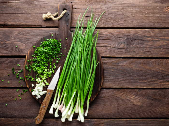 Chopped and full chives on a wooden cutting board