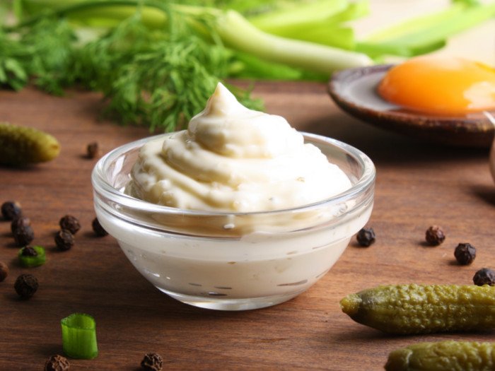 A bowl of homemade cream of tartar, pickles, parsley, dill, and mustard on a wooden table