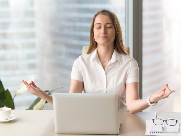 A woman sitting on her office desk and practicing deep breathing