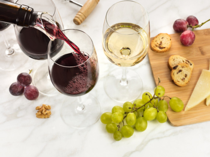 Glasses of red and white wine with grapes and cheese on the cutting board