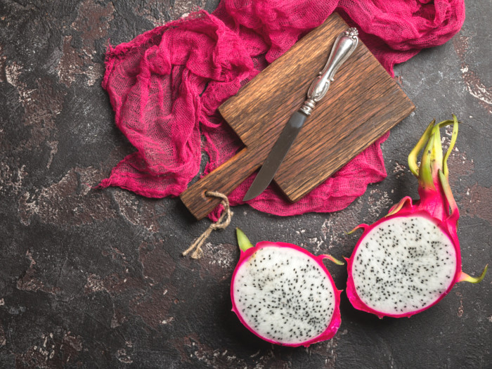 A sliced dragon fruit laid on a table with ra wooden board and knife on a red fabric