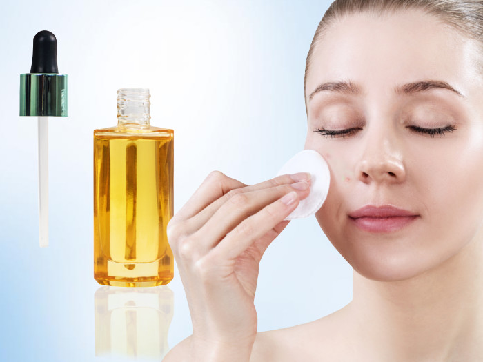 A young woman suffering from acne applying essential oil on her face