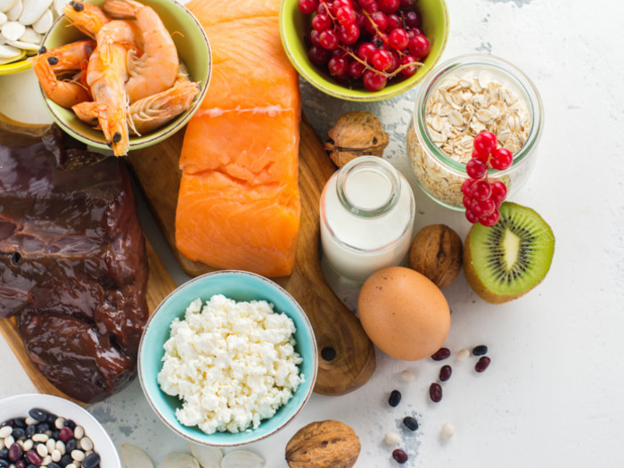 Flatlay picture of liver, fish, shrimps, egg, milk, fish, nuts, cheese, berries, and oats.