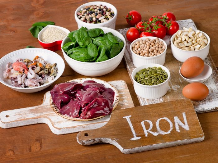 Iron rich foods (meat, fish, nuts, rice, pulses, cereals, eggs, tomatoes) on a wooden table