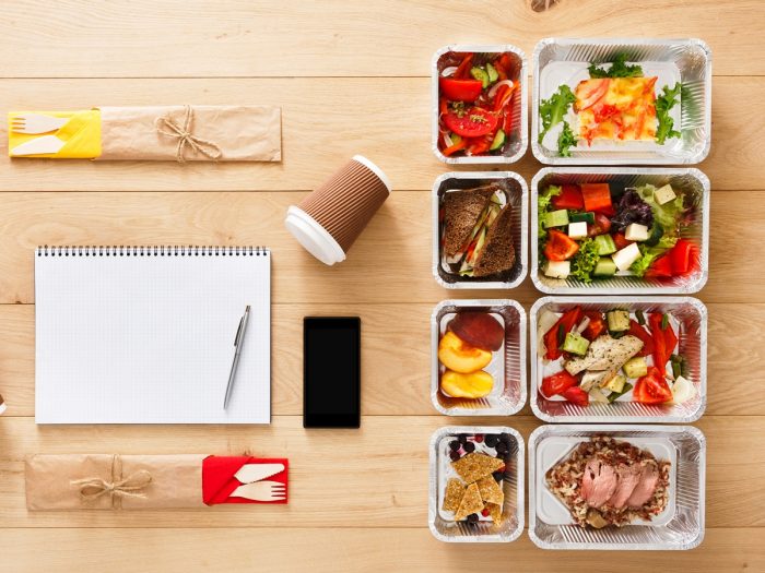 A folder, set of different meals, fork, spoons, and a cell phone neatly placed on a wooden table