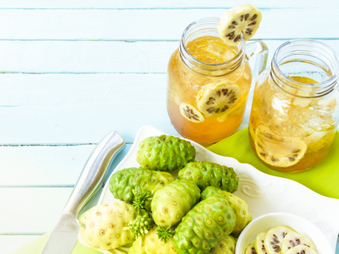 2 glasses of noni juice with noni fruits on a light blue background