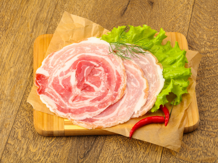 Pancetta on a parchment paper with lettuce and red chilies