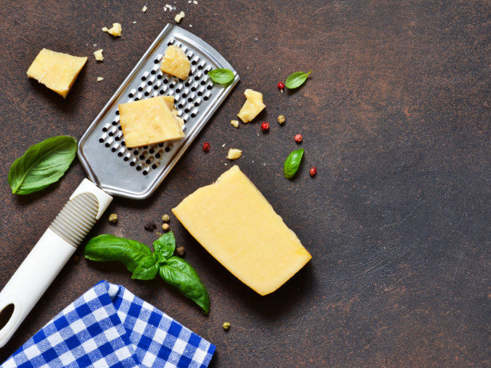 Flatlay pic of a black of cheese, grater, and basil leaves with a checked napkin on a slate surface
