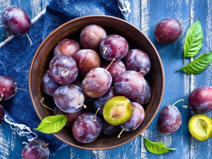 A basket with ripe plums with leaves on the blue table