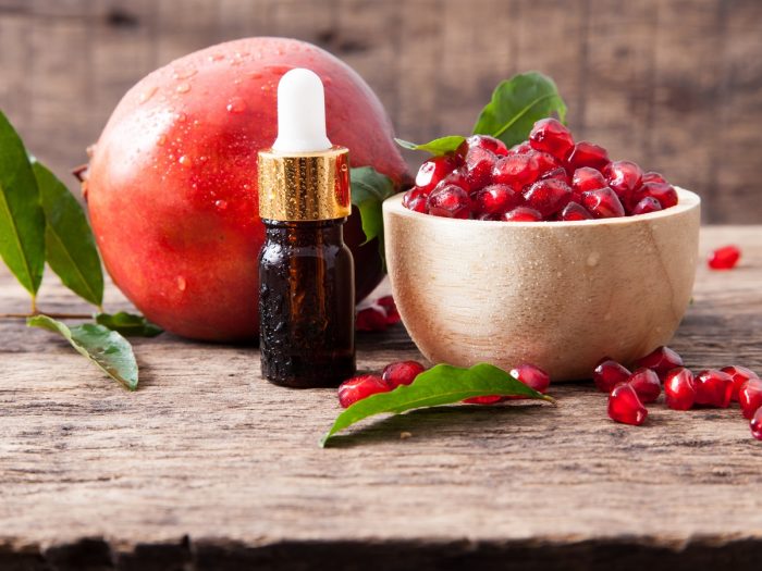 Fresh bowl of pomegranate seeds, bottle of oil, and whole pomegranate fruit on a table