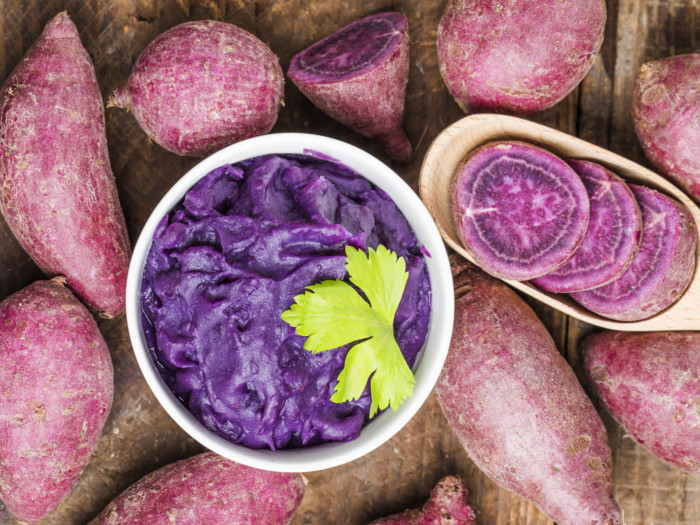 Purple potatoes spread on a table and a bowl of potato mash kept in th middle