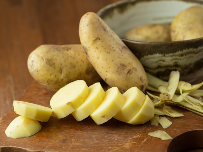 Whole and sliced potatoes with peels on a wooden background