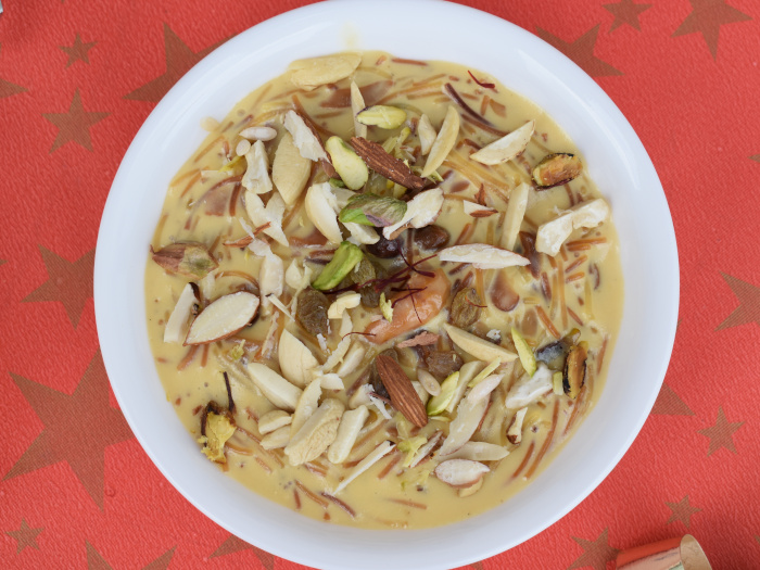 Sheer khurma with nuts in a white bowl against red background