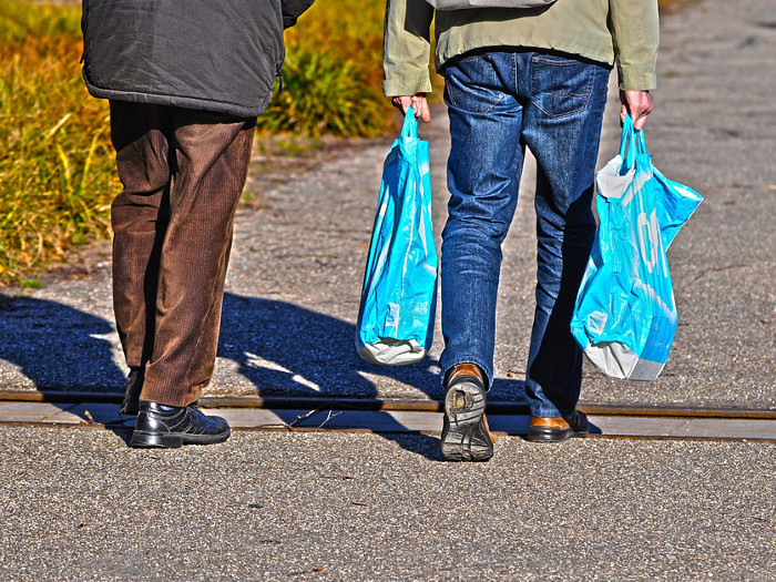 Two people walking on the street carrying plastic shopping bags