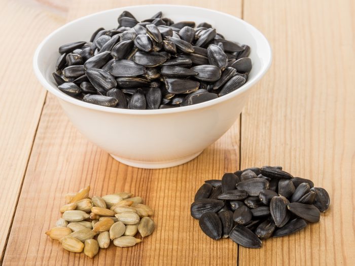 A bowl of dried sunflower seeds and peeled sunflower seeds on a wooden table