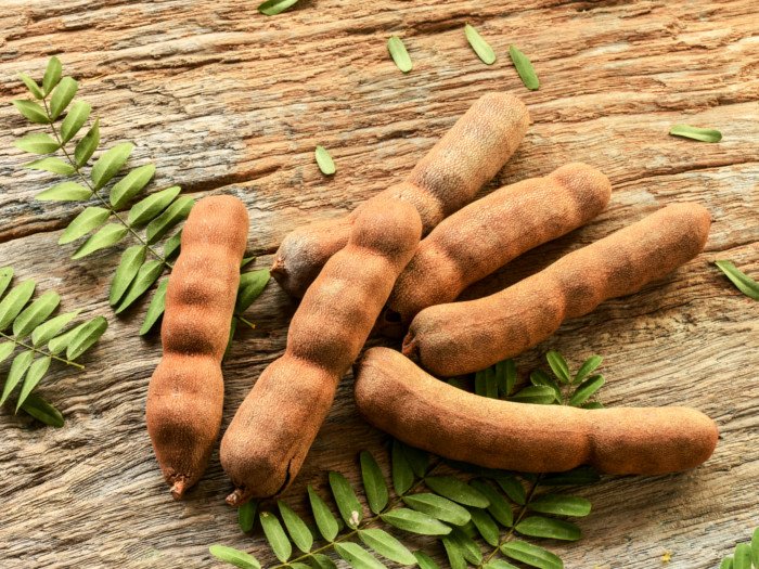 Sweet ripe tamarind pods with leaflets on a wooden background
