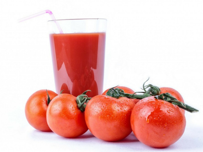 A glass of tomato juice with fresh and ripe tomatoes against a white background