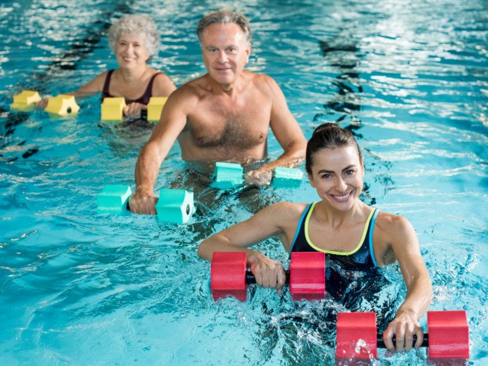 Trainer with senior citizens in a pool performing water exercises with weights