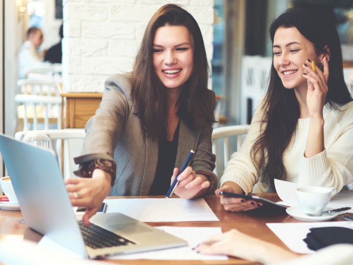 Two women smiling and working on laptops